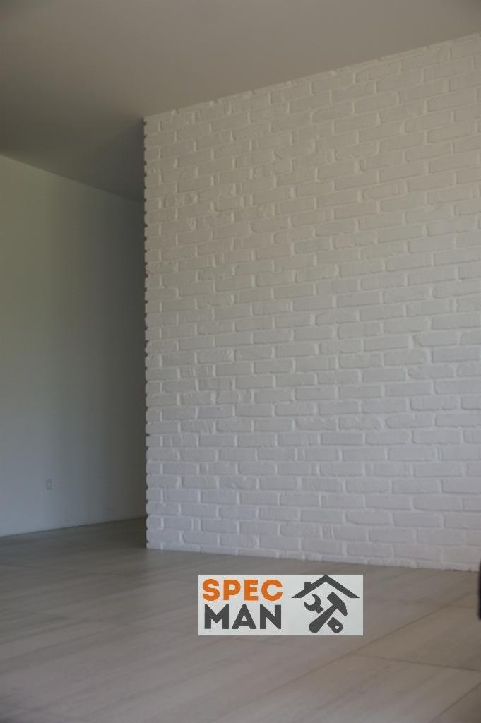 Ściana z białej cegły pomalowana na biało, z widocznym logo firmy na podłodze z paneli, minimalistyczne wnętrze.