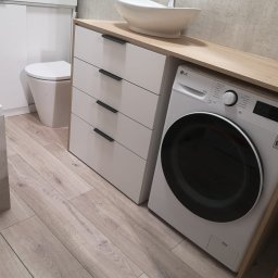 ERG INVESTMENTS Sp. z o.o. - Nowoczesna łazienka z białą umywalką nablatową, szafką z szufladami i pralką LG w zabudowie z blatem drewnopodobnym. Jasne drewniane panele podłogowe.
