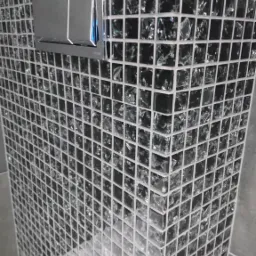 Ściana obłożona czarną mozaiką szklaną z chromowanym przyciskiem spłuczki, widok z dołu, fragment białej umywalki.