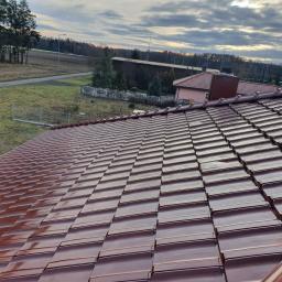 POKRYCIA DACHOWE - BARTŁOMIEJ LEŚNIAK - Nowy, błyszczący dach z dachówki ceramicznej w kolorze brązowym, widok z góry na tle krajobrazu wiejskiego z drzewami i budynkami w oddali.