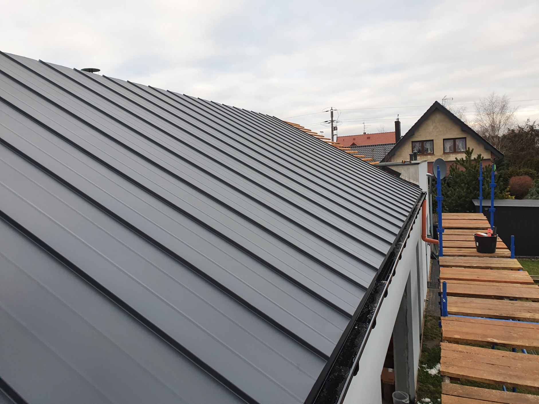 Nowy, grafitowy dach z blachy na budynku jednorodzinnym, widok z rusztowania, orynnowanie w kolorze czarnym.