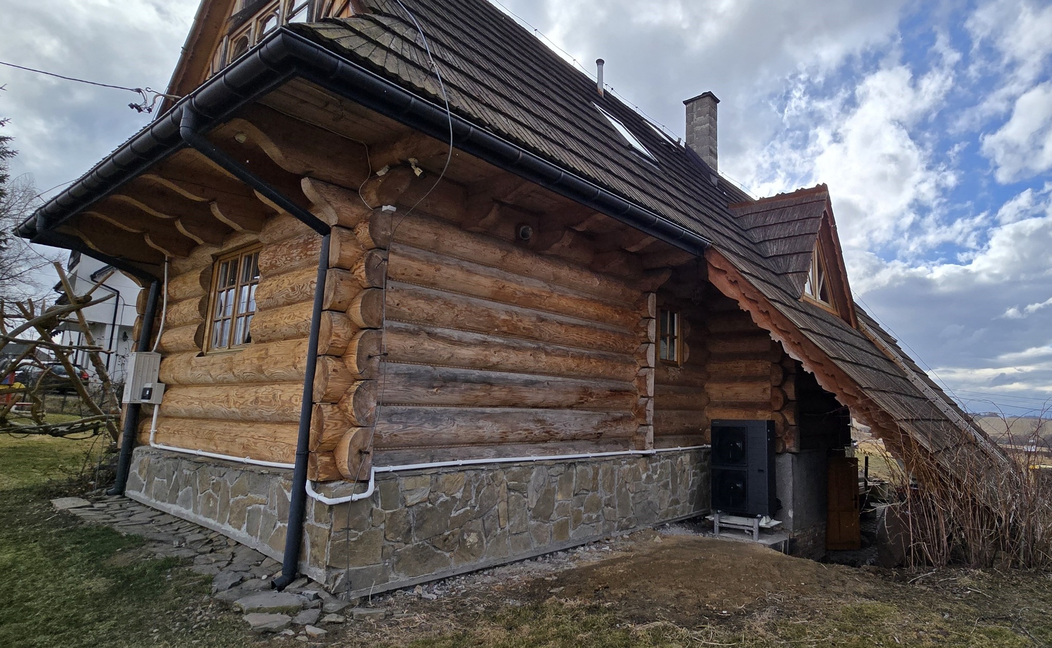 Drewniany dom w stylu góralskim z widoczną instalacją zewnętrzną i czarną skrzynką na zewnątrz, prawdopodobnie związaną z instalacjami.