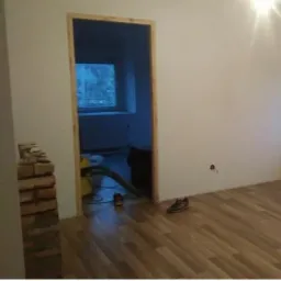 Porównanie stanu pokoju przed i po remoncie: po lewej stronie widok zniszczonego wnętrza z odpadającym tynkiem i bałaganem, po prawej odnowione wnętrze z nową podłogą, świeżo pomalowanymi ścianami...