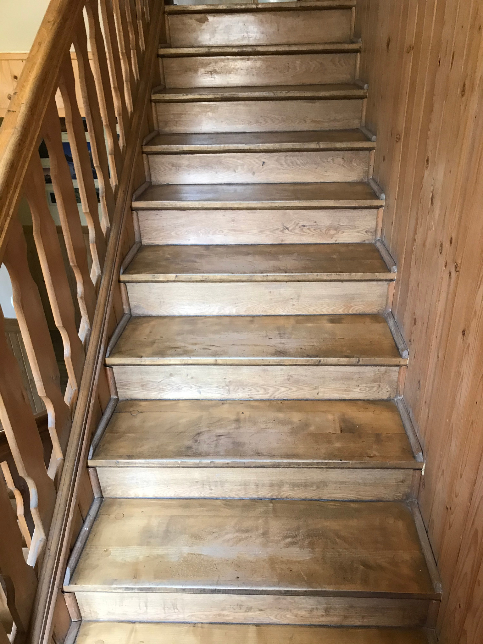 Drewniane schody z balustradą, widok z dołu, ślady użytkowania na stopniach, boazeria na ścianie.