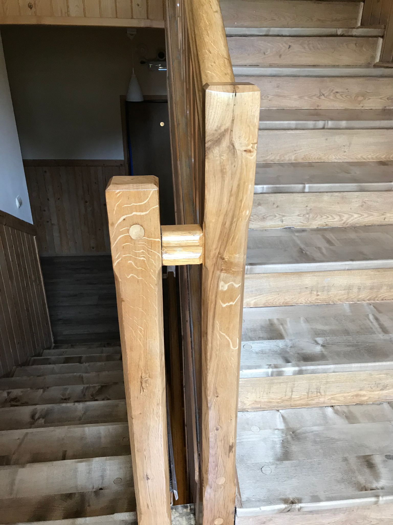 Drewniane schody z balustradą wykonane z jasnego drewna, widoczne sęki i naturalne usłojenie, fragment pomieszczenia w tle.