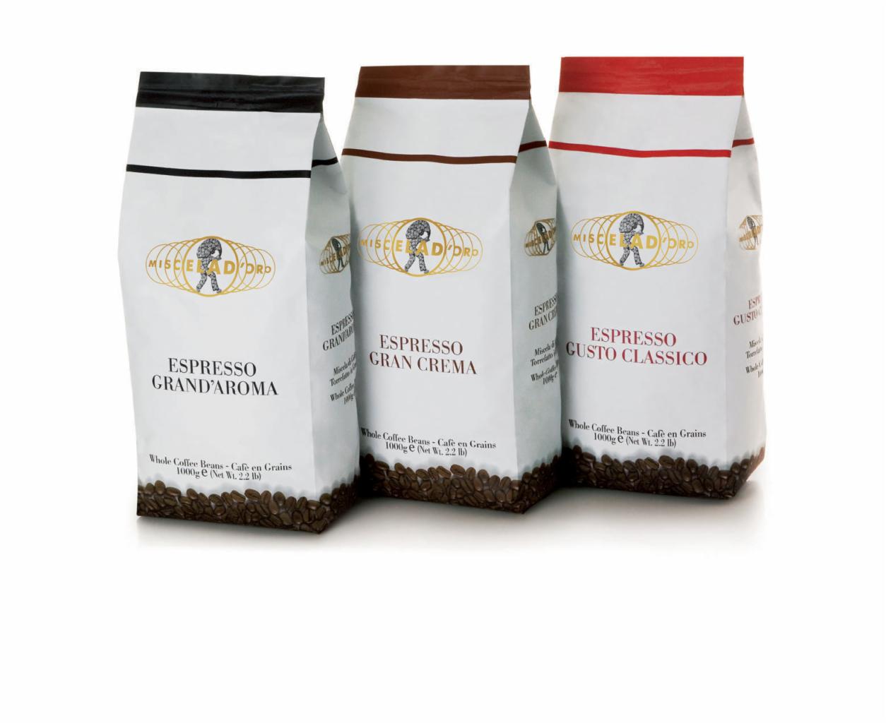 Trzy białe opakowania kawy ziarnistej Espresso Miscela D'Oro: Grand'Aroma, Gran Crema i Gusto Classico, ustawione obok siebie na białym tle.