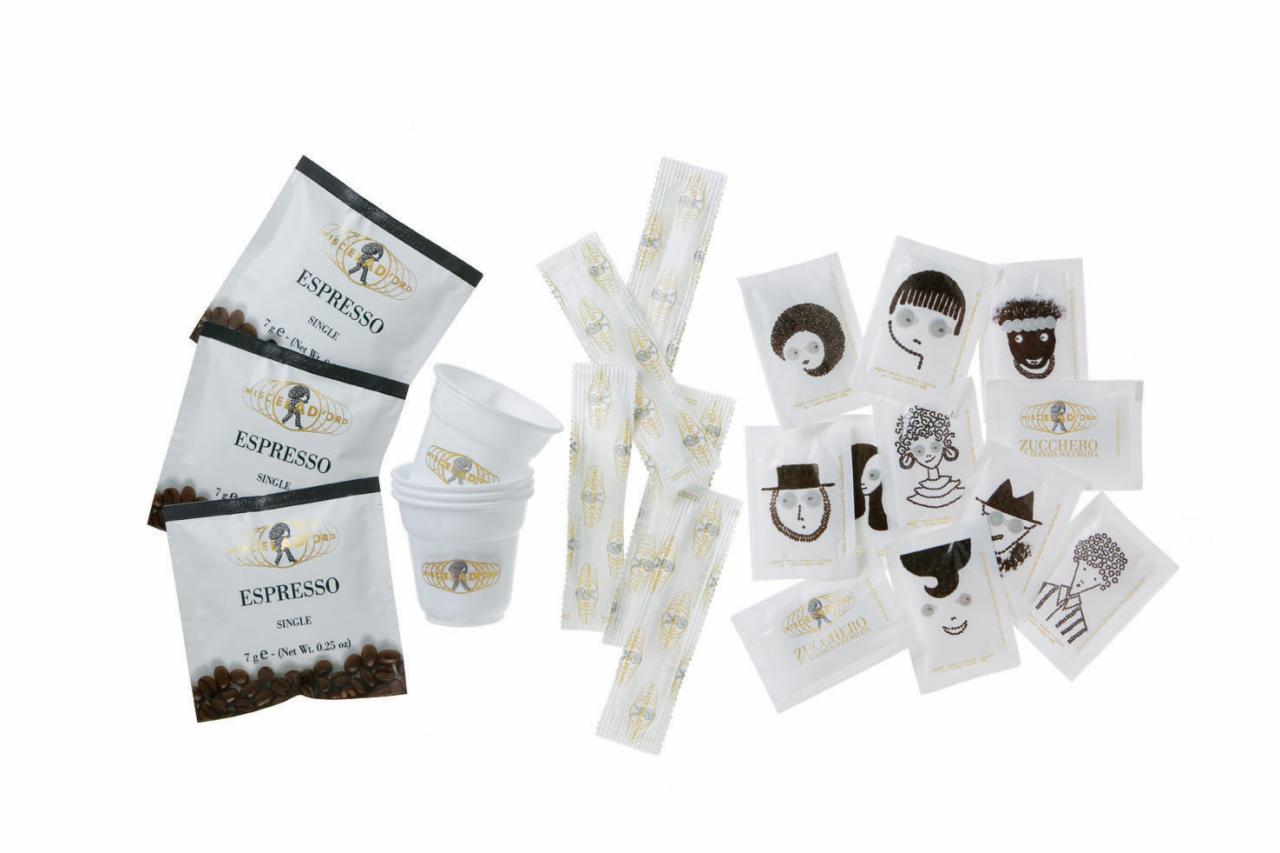 Zestaw startowy: trzy saszetki espresso z widocznymi ziarnami kawy, stosik plastikowych kubków, pojedynczo pakowane porcje cukru w ozdobnych opakowaniach z rysunkami twarzy oraz patyczki...