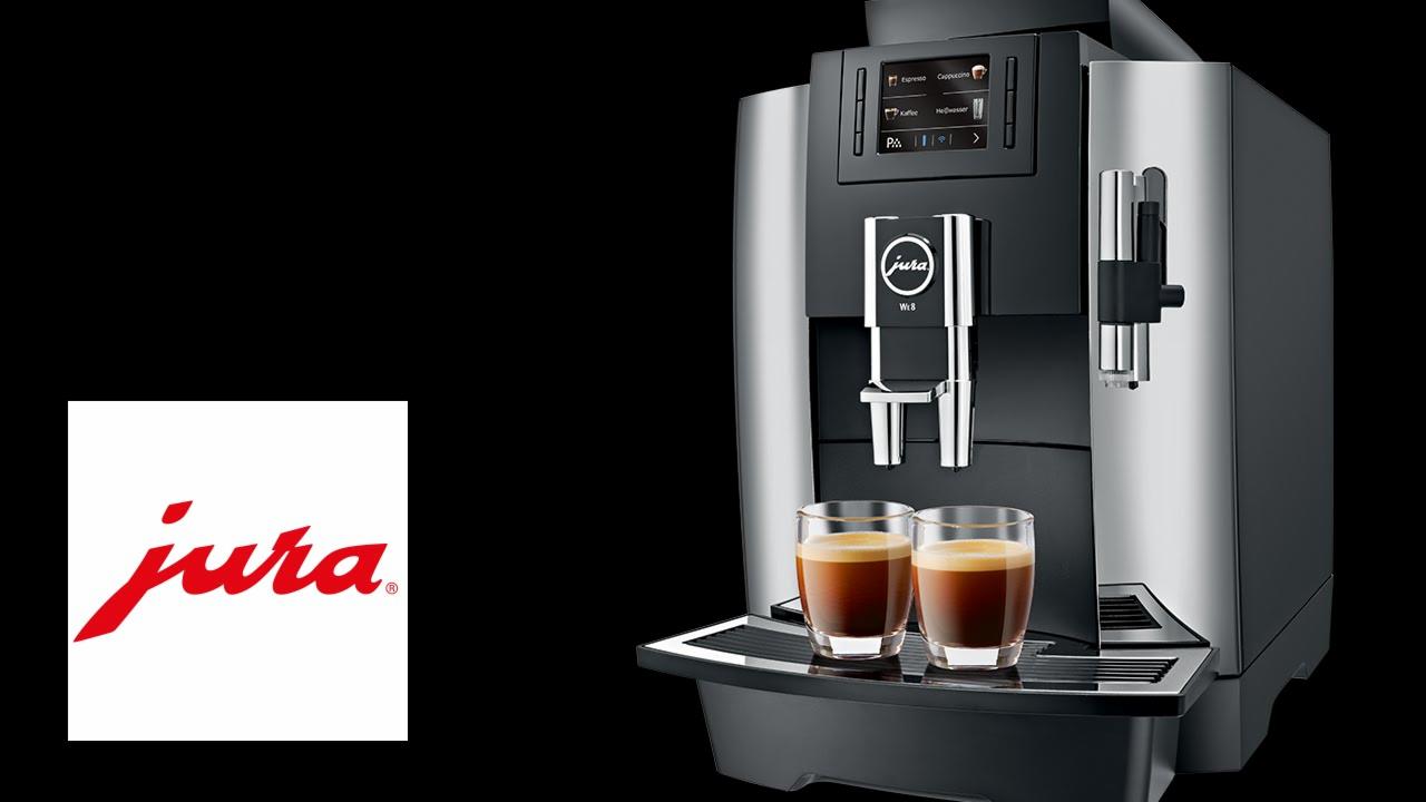 Automatyczny ekspres do kawy Jura WE8 z dwoma szklankami espresso na tacce, logo Jura w lewym dolnym rogu.