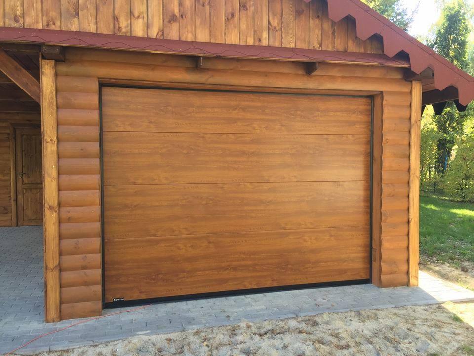 Zewnętrzna, segmentowa brama garażowa w kolorze drewna, z czarną ramą, zamontowana w drewnianym garażu, widok z zewnątrz.