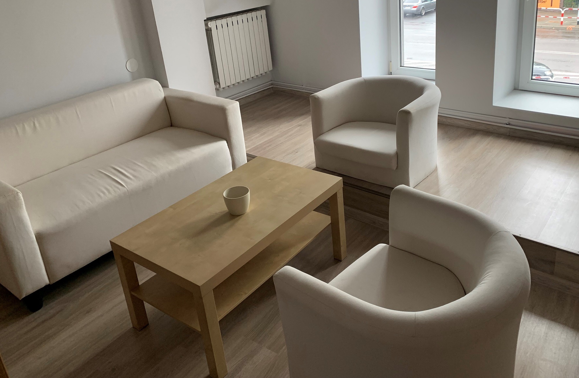 Jasne wnętrze biura z sofą, dwoma fotelami i stolikiem kawowym z kubkiem, widok z góry, drewniana podłoga.