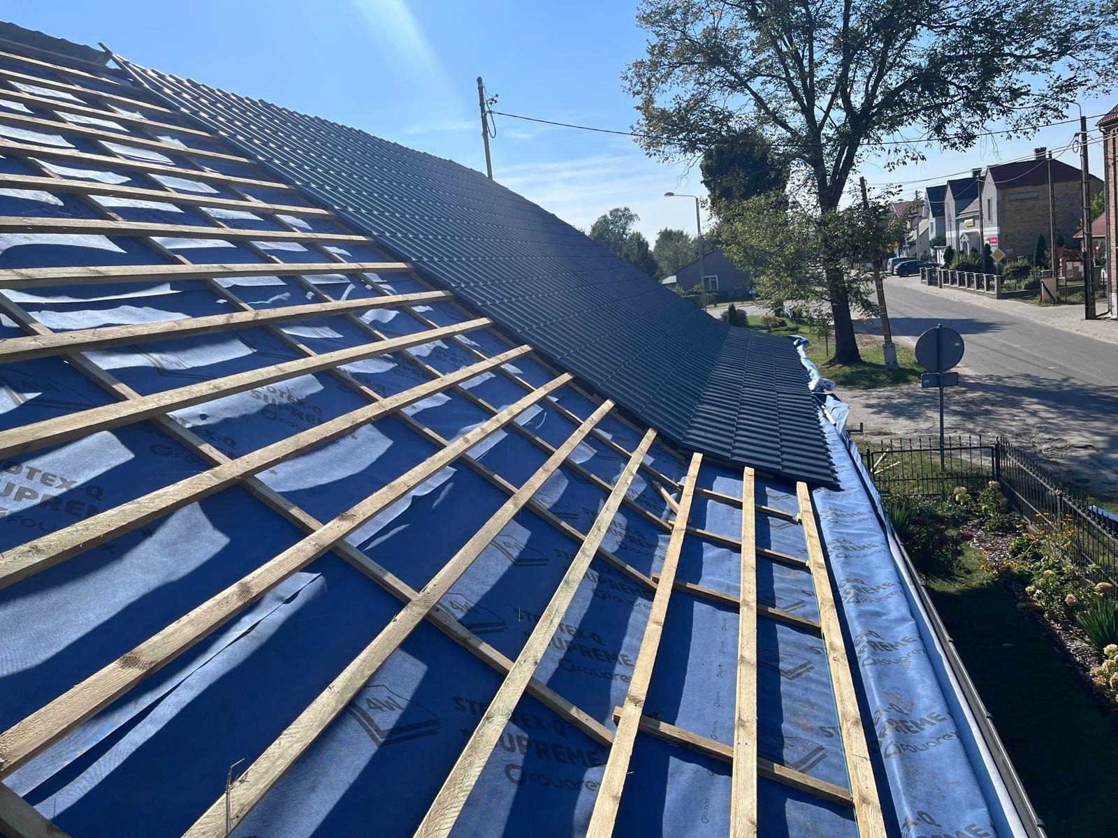 Montaż pokrycia dachowego z dachówki ceramicznej na konstrukcji więźby, widoczna membrana dachowa i częściowo ułożona dachówka w kolorze grafitowym.