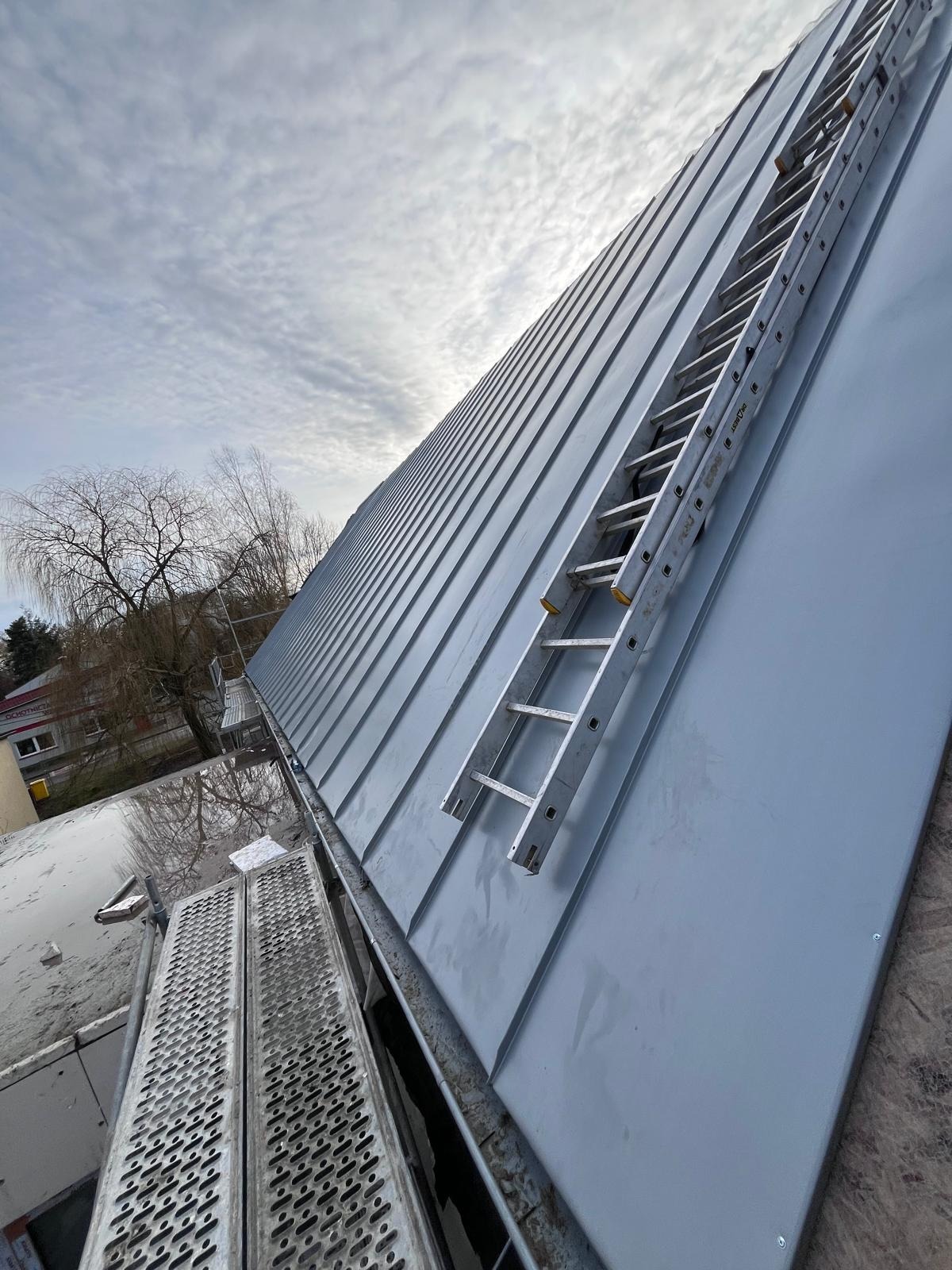 Metalowy dach z blachy trapezowej w trakcie montażu, drabina oparta o połać, widok z góry na konstrukcję dachu.