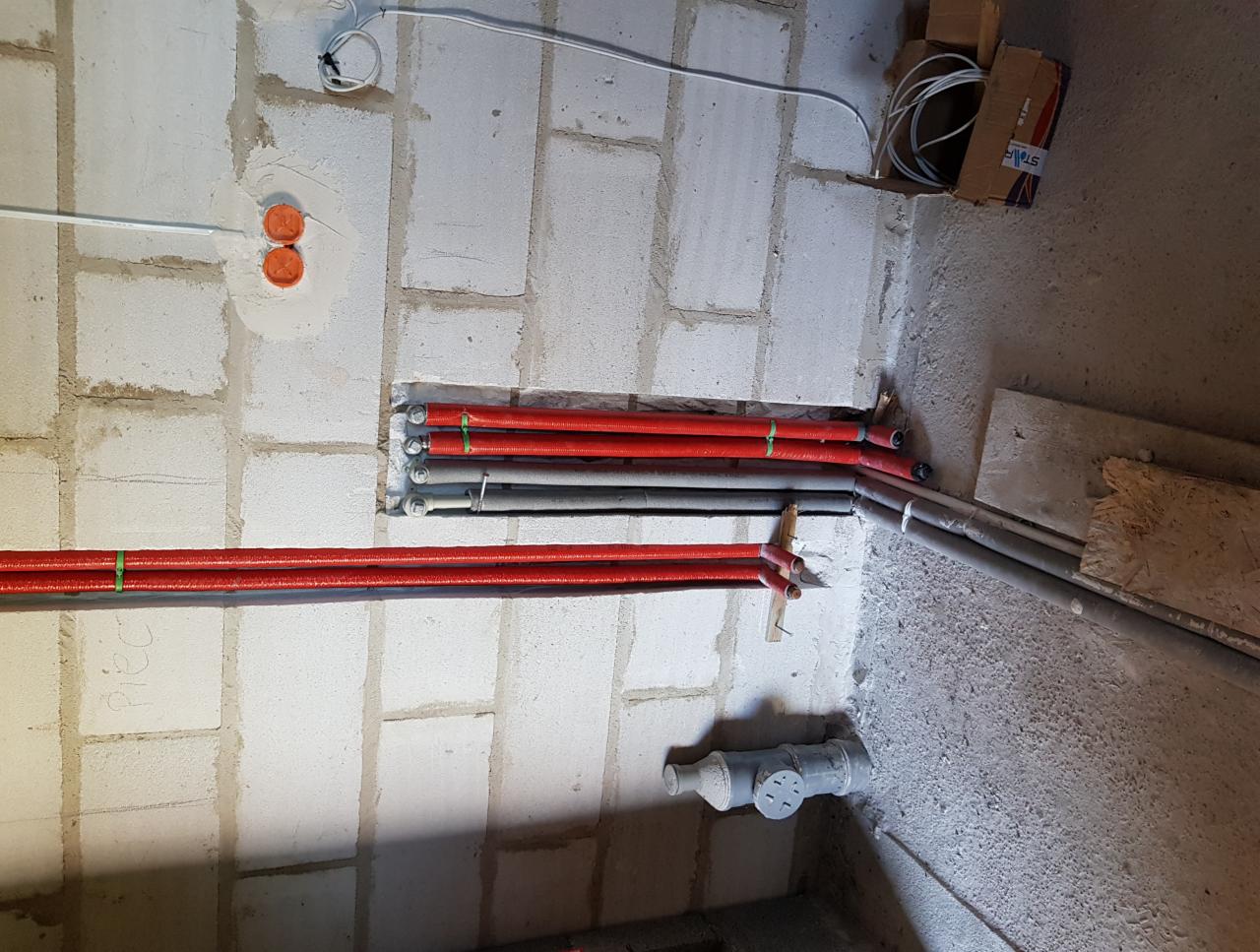 Instalacja hydrauliczna i elektryczna w surowym stanie: rury grzewcze w izolacji, peszle elektryczne i puszki podtynkowe w bloku z betonu komórkowego.