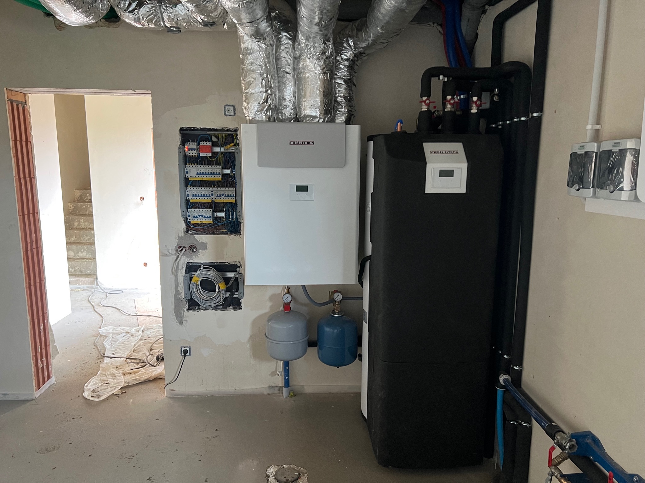 Wnętrze w stanie surowym z zamontowaną instalacją centralnego ogrzewania: zasobnik ciepłej wody użytkowej, pompa ciepła Stiebel Eltron, dwa naczynia wzbiorcze, rozdzielnica elektryczna i izolowane...