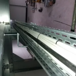 Metalowa konstrukcja wsporcza z ułożonymi wewnątrz białymi rurami instalacyjnymi, z widocznymi elementami mocującymi i narzędziami w tle.