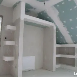 Wnętrze w trakcie remontu: zabudowa z profili i płyt, widoczne szpachlowane łączenia na skośnym suficie poddasza, przygotowane półki na ścianie