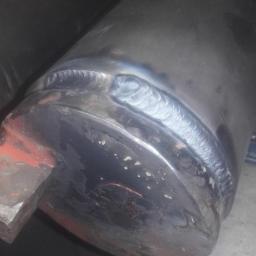 Oliweld - Spoina na metalowej rurze, widoczna struktura spawu, zarysowania i ślady użytkowania na powierzchni.