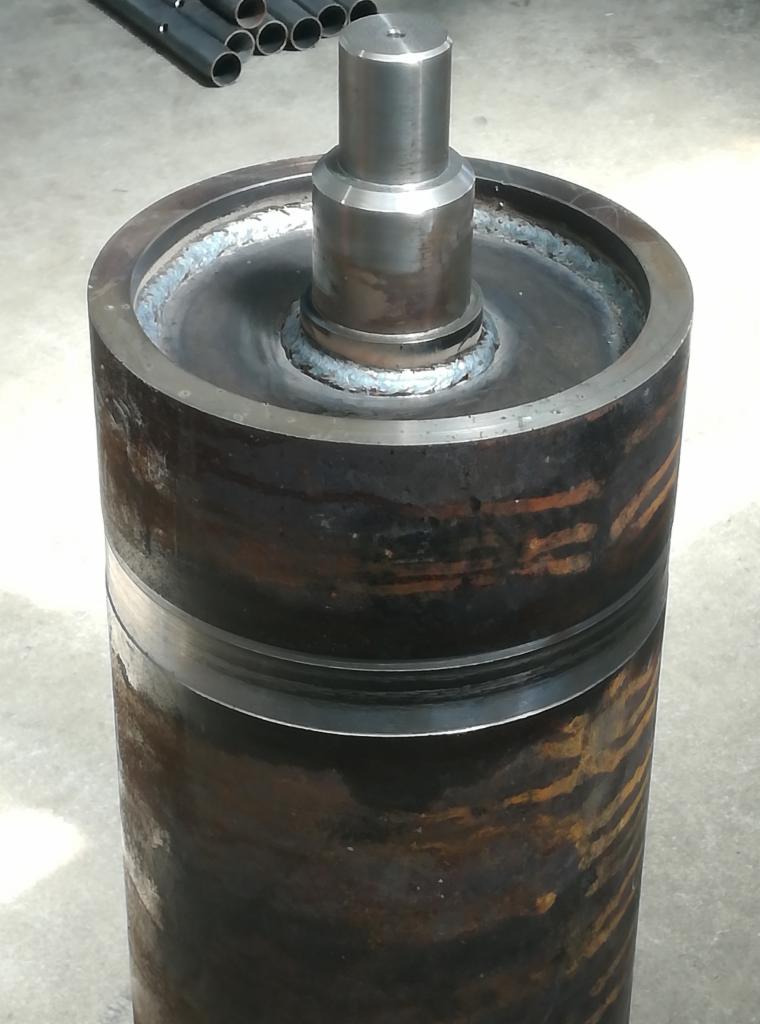 Cylindryczny metalowy element z przyspawanym trzpieniem, widoczne ślady rdzy i spawania.