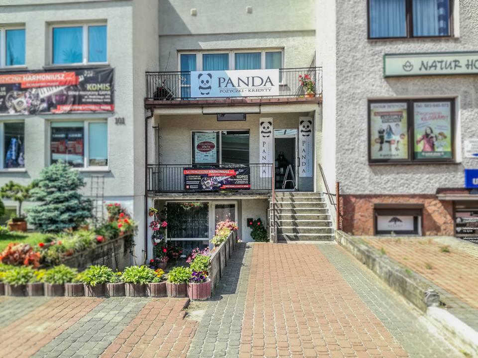 Fasada budynku z szyldem 'PANDA Pożyczki - Kredyty' nad wejściem i na balustradzie, widok z zewnątrz z chodnika wyłożonego kostką brukową.