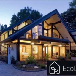 Nowoczesny dom z dużymi przeszkleniami i charakterystycznym dachem dwuspadowym, oświetlony z zewnątrz, widoczny ogród i brama wjazdowa, w prawym dolnym rogu logo firmy Ecodomy.