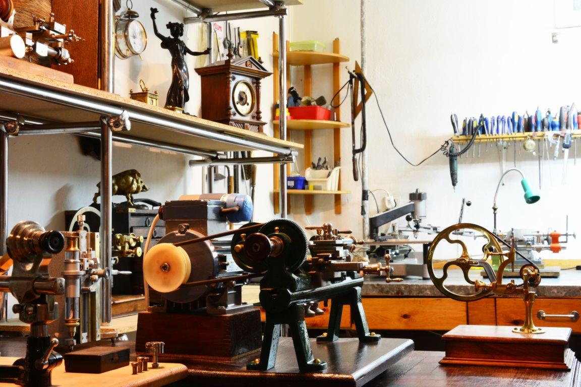 Warsztat w Łodzi z różnorodnymi tokarkami i narzędziami do obróbki metali, widoczne zegary i figurka na półkach w tle.