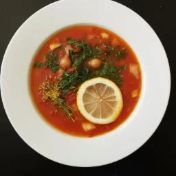 Apetyczna zupa pomidorowa w białym talerzu, udekorowana plastrem cytryny, świeżym koperkiem i młodymi cebulkami, na czarnym tle.