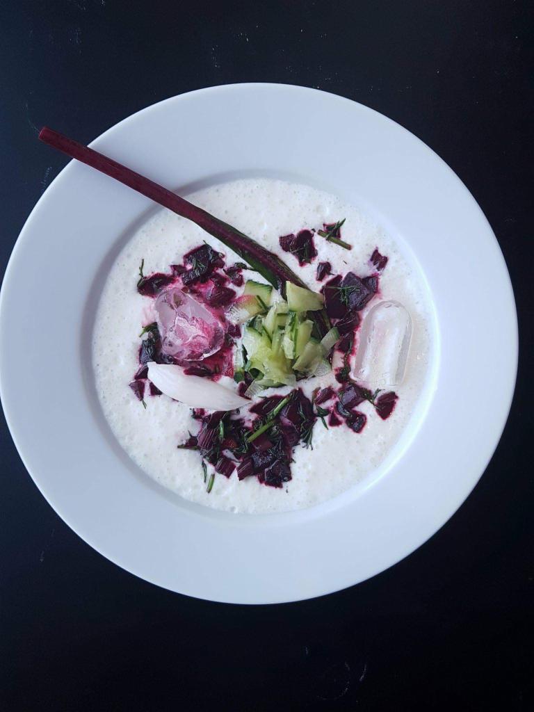 Chłodnik litewski z burakiem, ogórkiem, kefirem, kostkami lodu i łodygą buraka na białym talerzu, widok z góry na czarnym tle.