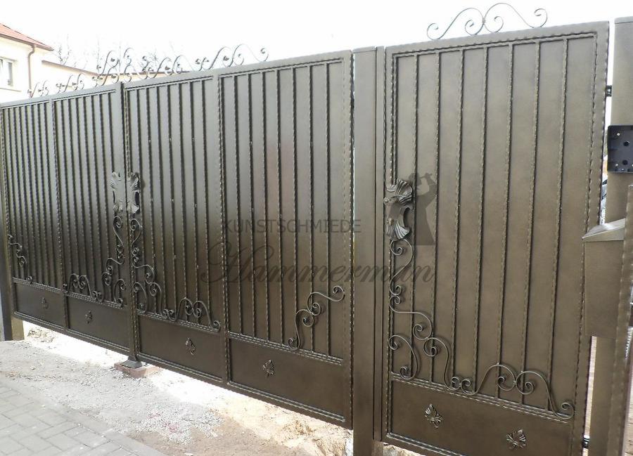 Metalowa brama wjazdowa z dekoracyjnymi elementami kutymi, w kolorze ciemnego brązu, ozdobiona motywem lwa na klamce, widoczna z perspektywy ulicy.