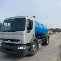 Srebrna ciężarówka Renault z niebieskim zbiornikiem cysterną na podwoziu, stojąca na asfaltowej drodze w słoneczny dzień.