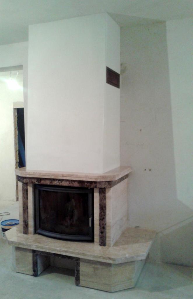 Nowoczesny kominek z obudową z jasnego marmuru w trakcie montażu w Obornikach, widoczne niedokończone wykończenie ściany i fragment pomieszczenia w tle.