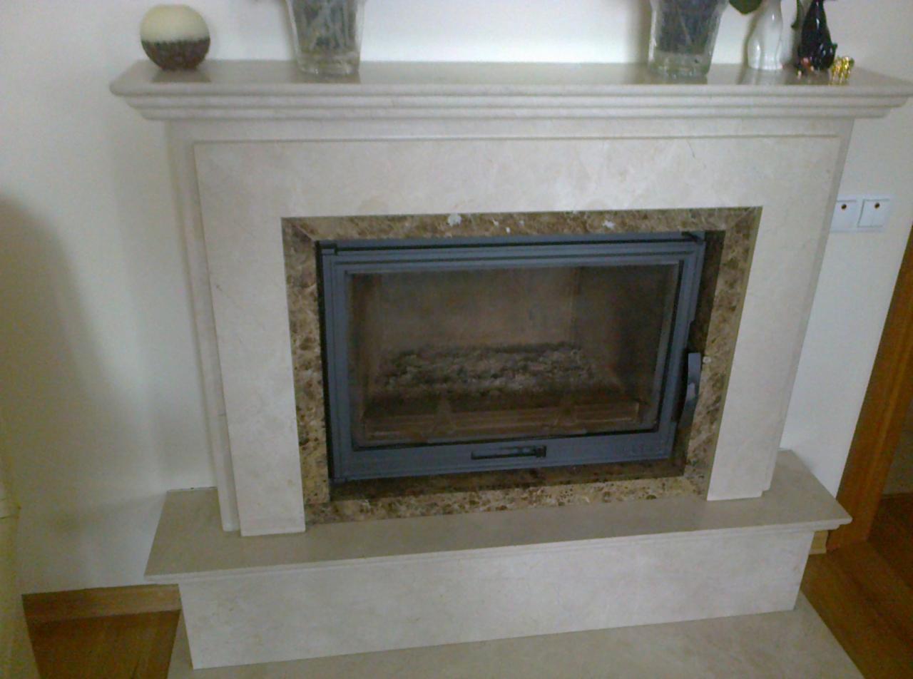 Marmurowy kominek z zamkniętym paleniskiem, na górnej półce dekoracje, widoczne ślady użytkowania wewnątrz paleniska.