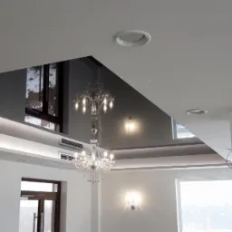 Nowoczesne wnętrze z lustrzanym sufitem napinanym w kształcie trapezu, oświetlonym listwą LED i kryształowym żyrandolem, widoczne okna i klimatyzacja.