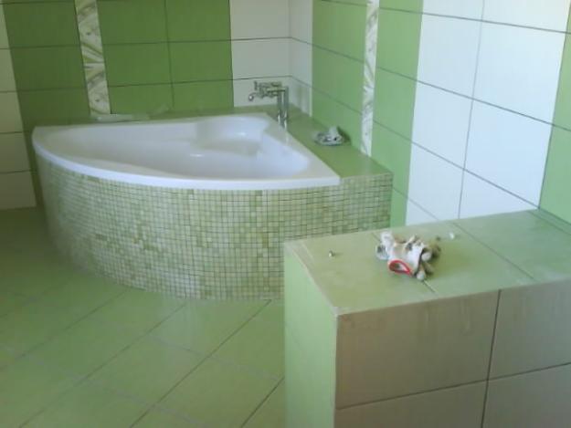 Wykończona łazienka w odcieniach zieleni i bieli, z narożną wanną obłożoną mozaiką, widoczne narzędzia na blacie.