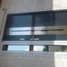 Nowoczesne, szare drzwi wejściowe z poziomymi, srebrnymi akcentami, osadzone w surowym murze z widoczną taśmą uszczelniającą wokół ramy.