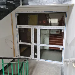 Nowe białe drzwi wejściowe z przeszkleniami, zamontowane w klatce schodowej, zabezpieczone niebieską folią malarską, widok z góry ze schodów.