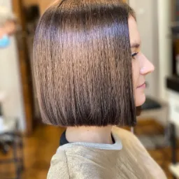 Gładkie, ciemnobrązowe włosy ścięte w klasycznego boba, widok z profilu, delikatny makijaż oczu.