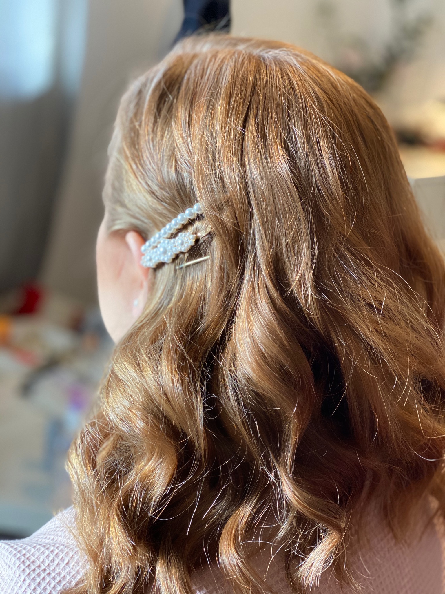 Widok z tyłu na upięte, falowane, miedziane włosy z ozdobną spinką z pereł.
