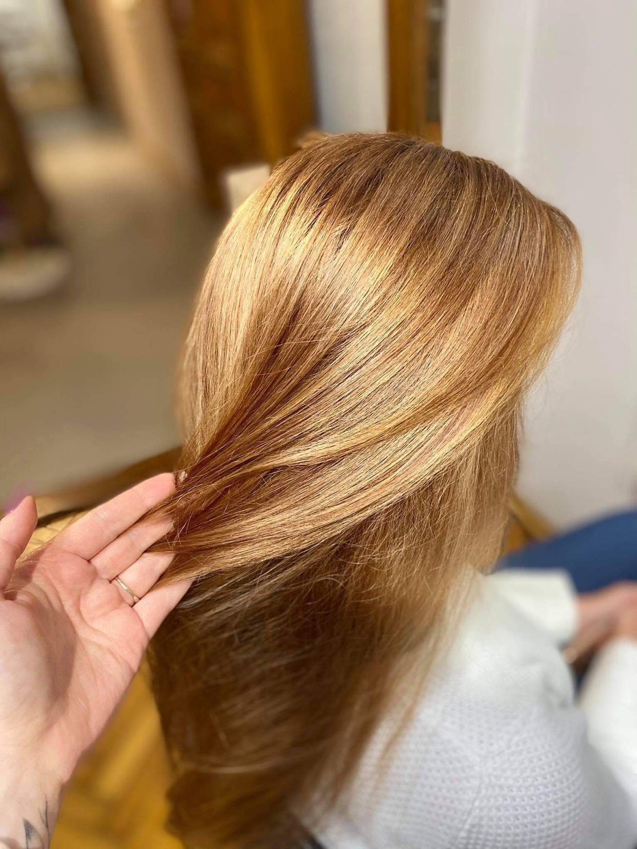 Świeżo farbowane, lśniące, miedziano-złote włosy, delikatnie przytrzymywane dłonią z pierścionkiem, ukazujące wielowymiarowość koloru.