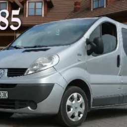 Srebrny van Renault Trafic z numerem telefonu na tle budynku w stylu rustykalnym.