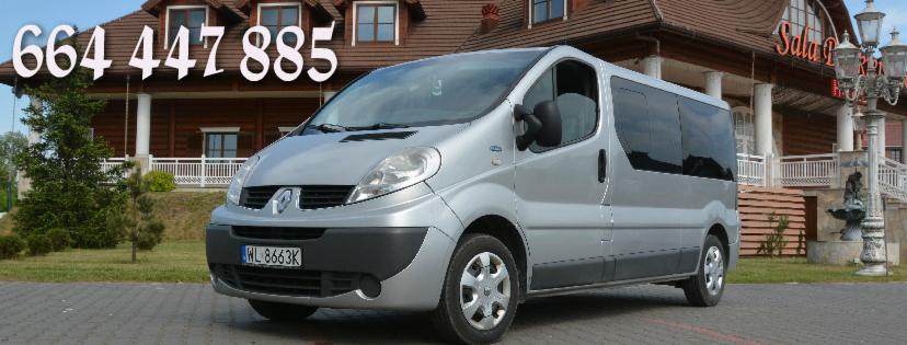 Srebrny van Renault Trafic z numerem telefonu na tle budynku w stylu rustykalnym.