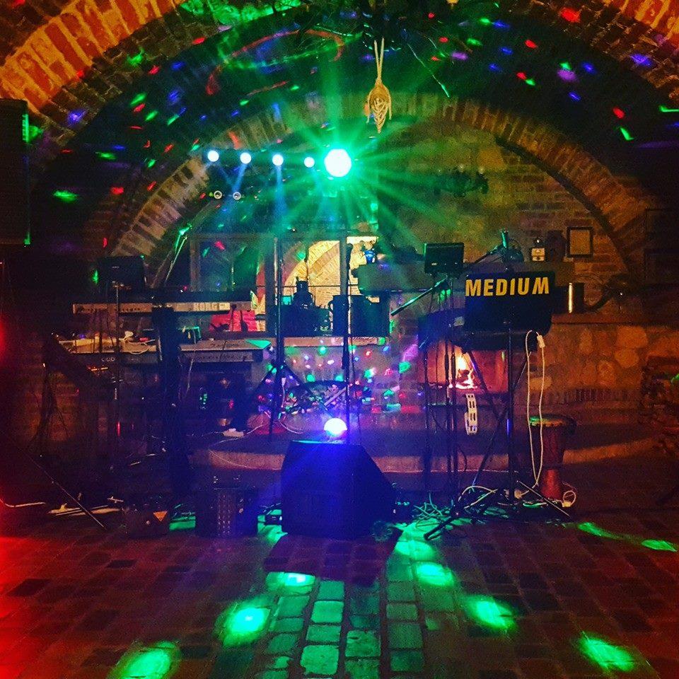 Zespół muzyczny na scenie z instrumentami klawiszowymi, oświetleniem disco i ceglanym sklepieniem w tle, przygotowany do występu.