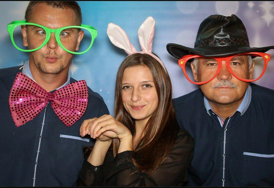 Trzy osoby w przebraniach pozują do zdjęcia na tle dekoracji imprezowej: mężczyzna z zezem w zielonych okularach i różową muszką, kobieta w opasce z króliczymi uszami oraz mężczyzna w kowbojskim...