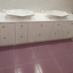 Biała szafka łazienkowa na wymiar z dwoma umywalkami w kształcie diamentu i ozdobnymi kryształowymi gałkami, na tle białych płytek z falistym wzorem i fioletowej podłogi.