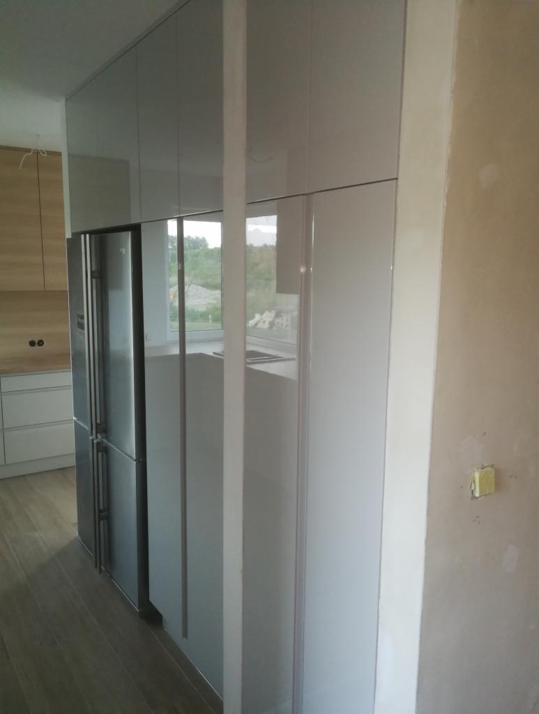 Kuchnia na wymiar w Twardogórze w trakcie montażu: widoczne białe, lakierowane fronty szafek i zabudowana lodówka, ściana wymaga wykończenia.