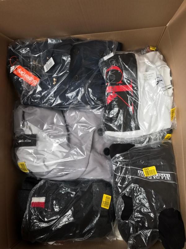 Kartonowe pudło wypełnione różnorodną odzieżą markową zapakowaną w foliowe torby, widoczne logo Superdry, Calvin Klein, Napapijri i Tommy Hilfiger.