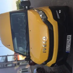 Żółty samochód dostawczy marki Iveco z polską tablicą rejestracyjną EL-1G749, zaparkowany na zewnątrz budynku.