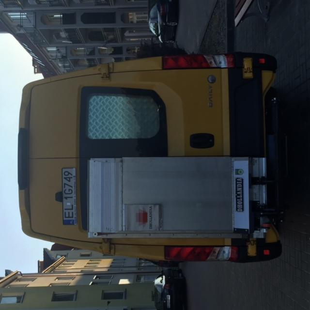 Żółty bus dostawczy z podnośnikiem z tyłu, zaparkowany na ulicy, widok z tyłu na otwarty podnośnik i tablicę rejestracyjną EL 1G749.