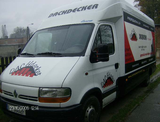 Biały samochód dostawczy z logo firmy dekarskiej 'DACHdecker' na masce i boku, oraz reklamą usług dekarskich na tylnej części nadwozia, zaparkowany na ulicy.