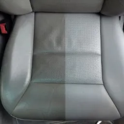 Szare skórzane siedzenie samochodowe z wyraźnym podziałem na część wyczyszczoną i zabrudzoną, widoczne perforacje i boczne elementy wnętrza pojazdu.