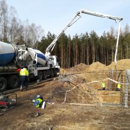 Pro-Builder Paweł Szymański - Betonowa pompa podaje mieszankę do szalunków zbrojeniowych na placu budowy, w tle las i niebo.